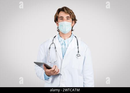 Serious male doctor with mask holding digital tablet Stock Photo
