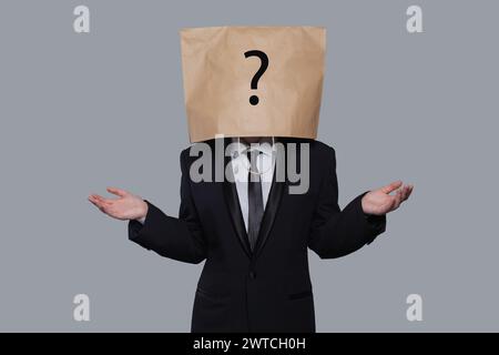 Paper bag head business person with question mark standing with empty open palm hands on gray background Stock Photo