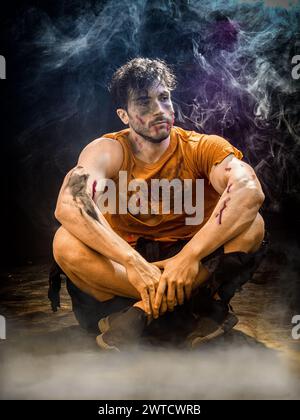A zombie man is seated on the ground with his hands crossed over his chest. He appears deep in thought or contemplation, looking straight ahead. The background is simple and unobtrusive. Stock Photo