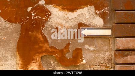 weathered orange wall with a white arrow pointing left, indicating a turn or detour Stock Photo