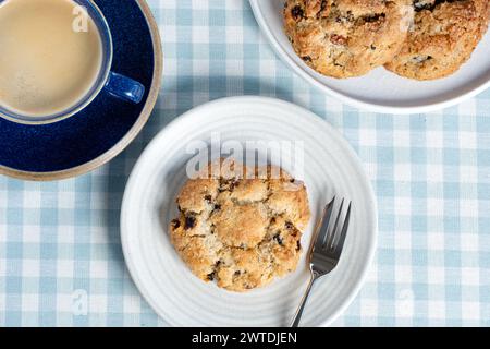 A fresh traditional large, English, Rock cake served with a cup of black coffee. The cakes are plated with a pastry fork on a chequered table cloth Stock Photo