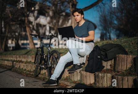 Active man with bicycle takes a break in the park to work on laptop Stock Photo