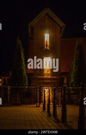 Illuminated chapel in a small town, night view, highlighted figurines of saints Stock Photo