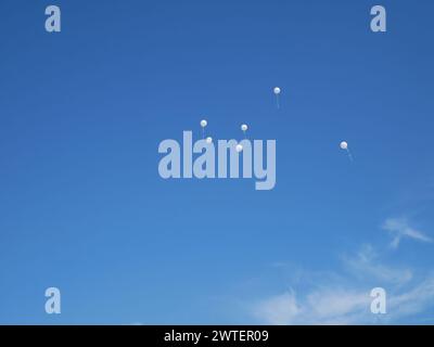 Several white balloons rise up against the background of a blue almost cloudless sky Stock Photo