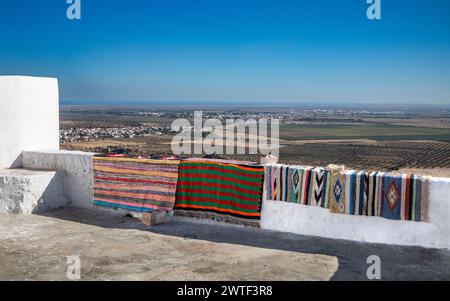 Traditional hand-woven woollen rugs with the city of Enfidha and the Mediterranean Sea seen from the ancient hilltop Berber village of Takrouna, Tunis Stock Photo