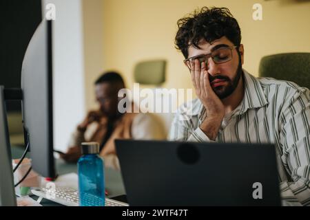Tired male employee rubbing his eyes after hard day at work. Stock Photo