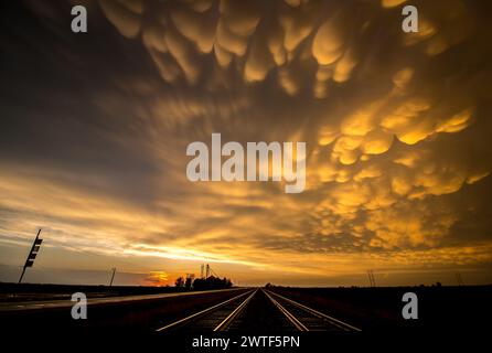 Mammatus clouds fill the sky after a passing storm at sunset. Railroad tracks extend to the horizon. Stock Photo