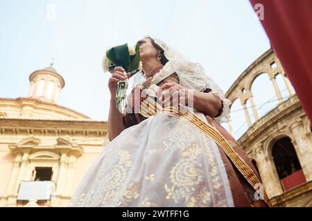A fallera dressed in traditional costume is walking past the Plaza de la Virgen to offer flowers to Saint Mary during the Las Fallas Festival in Valencia, Spain, on March 17, 2024. The Fallas is Valencia's most international festival, which is taking place from March 15 until March 19. The Las Fallas festivities are celebrating the arrival of spring with fireworks, fiestas, and large cardboard monuments called Ninots. The festival has been designated as a UNESCO Intangible Cultural Heritage of Humanity since 2016. (Photo by David Aliaga/NurPhoto) Stock Photo