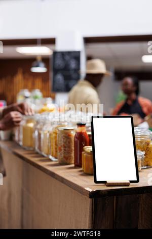 Close-up of phone tablet displaying an isolated copyspace template is seen at an eco friendly food shop. Focused image of a digital device with an empty mockup display, placed near bio-food products. Stock Photo