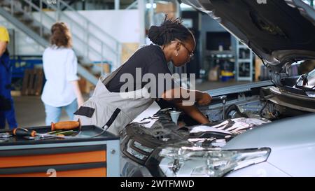 Qualified repairman in garage using torque wrench to tighten bolts inside opened up vehicle, preparing to change oil. Auto repair shop expert doing checkup on car using professional tools Stock Photo