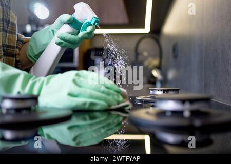 Hand in a green rubber glove washes the gas stove. Cleaning the kitchen. Stock Photo