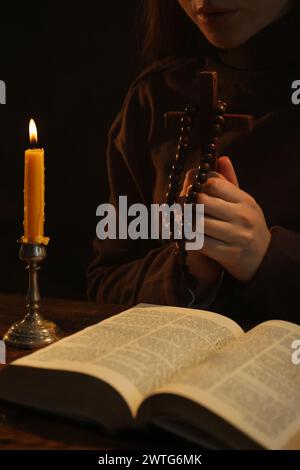 Woman praying at table with burning candle and Bible, closeup Stock Photo