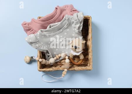 Different baby accessories and clothes in wicker box on light blue background, top view Stock Photo