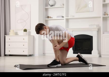 Man suffering from leg pain on mat at home Stock Photo