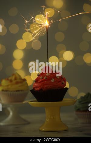 Delicious cupcake with sparkler on table against blurred lights Stock Photo