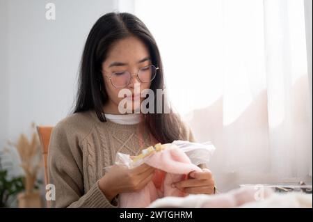 A focused young Asian woman threading a pattern on an embroidery frame, hand-sewing on cloth. Handmade needlework, hobby, handmade, handcraft Stock Photo