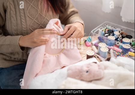 A close-up image of a woman using scissors to cut a thread on an embroidery frame, hand-sewing a pattern on cloth, crafting handmade items. needlework Stock Photo