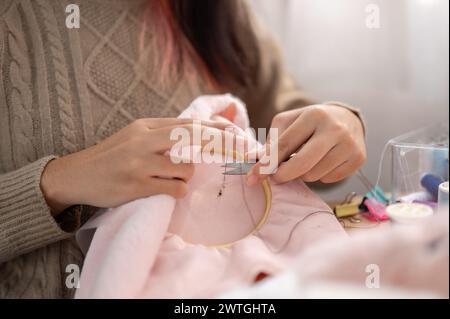 A close-up image of a woman using scissors to cut a thread on an embroidery frame, hand-sewing a pattern on cloth, crafting handmade items. needlework Stock Photo