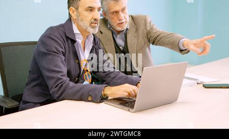 Partners discussing which workers they will dismiss while using laptop Stock Photo