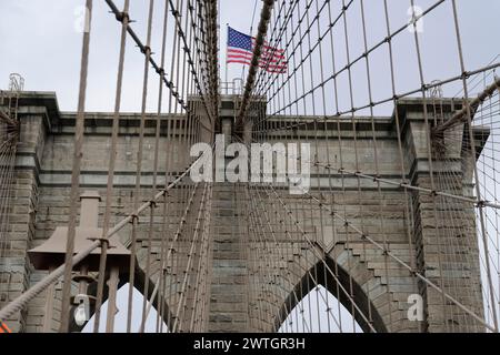 Bridge piers of the Brooklyn Bridge with complex ropework and USA flag in the background, Manhattan, New York City, New York, USA, North America Stock Photo