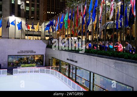 People watching the ice skating rink in Rockefeller Plaza, surrounded by flags, Manhattan, New York City, New York, USA, North America Stock Photo