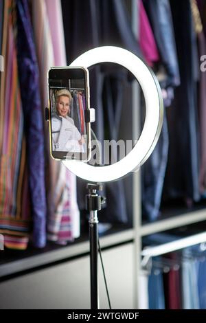 Beautiful mature woman, stylist Social media influencer and video blogger, records a video on her phone about clothing and fashion style in a wardrobe Stock Photo