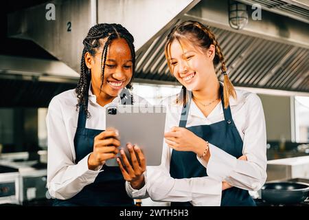 In a big professional kitchen two famous chefs use a tablet to discuss their video blog Stock Photo