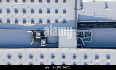 Drone photography of a large building rooftop with skylights covered by snow and air conditioning units during winter sunny day Stock Photo