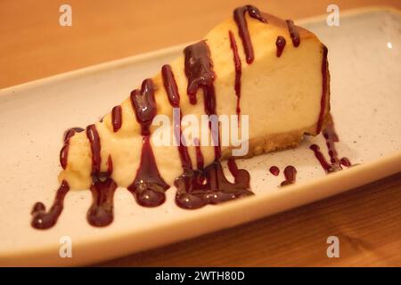 A slice of cheesecake with a chocolate sauce drizzled on top. Stock Photo