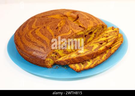 A slice of cake with a blue plate on a white background. The cake is cut in half and has a zigzag pattern Stock Photo