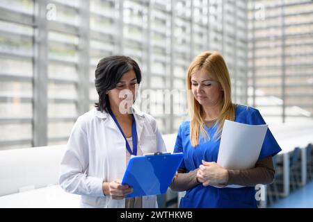 Two female doctors discussing test results, patients diagnosis. walking across corridor. Women in medicine science Stock Photo