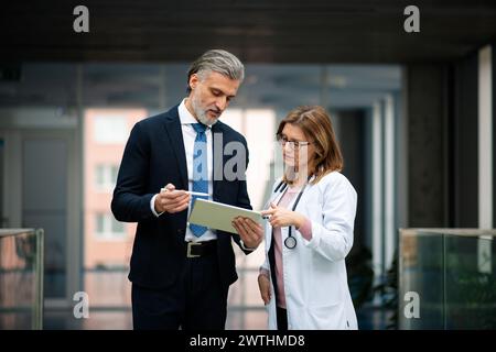 Doctor talking to pharmaceutical sales representative, presenting new medication. Hospital manager talking with female doctor. Side view with Stock Photo