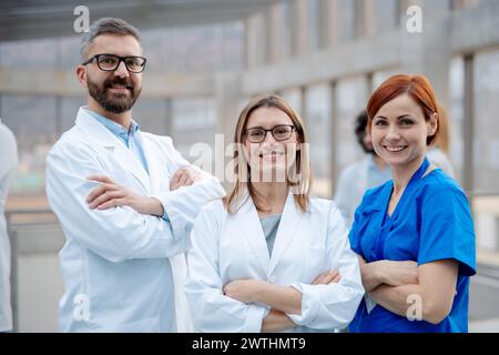 Portrait of three doctors, looking at camera, smiling. Healthcare team in medical uniforms in hospital. Stock Photo