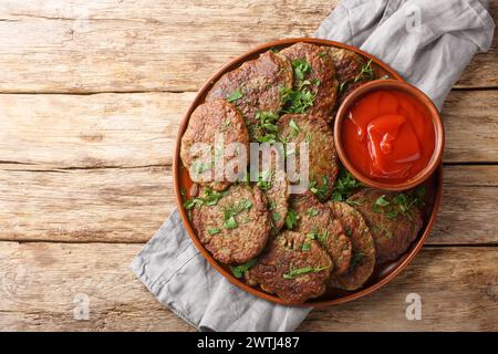 Delicious dietary liver patties served with tomato sauce and herbs close-up in a plate on the table. Horizontal top view from above Stock Photo