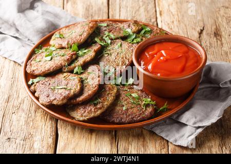 Delicious dietary liver patties served with tomato sauce and herbs close-up in a plate on the table. Horizontal Stock Photo