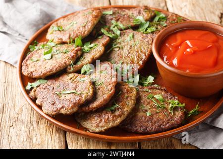 Spicy liver pancakes served with tomato sauce and herbs close-up in a plate on the table. Horizontal Stock Photo