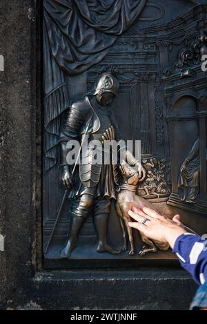 Tourist touches dog on Bronze below the statue of St, John of Nepomuk on Charles bridge, Prague, Czech Republic Stock Photo