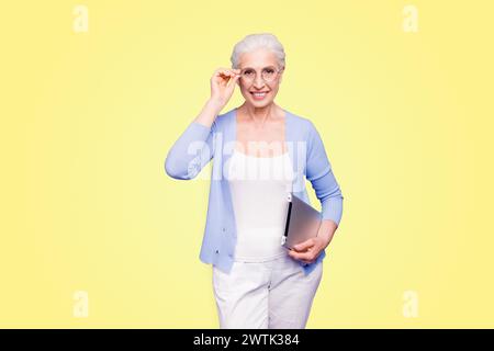 Grey haired old smiling business woman wearing glasses, holding tablet. Isolated over violet purple background Stock Photo