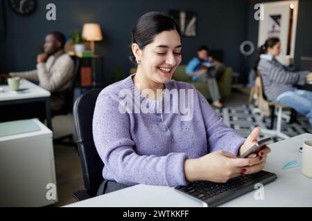 Portrait of smiling Middle eastern woman using smartphone and having fun playing mobile games at workplace or reading text messages Stock Photo