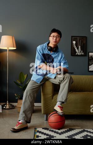 Vertical full length portrait of Asian young man working from home or in office lounge and looking at camera playing with basketball Stock Photo