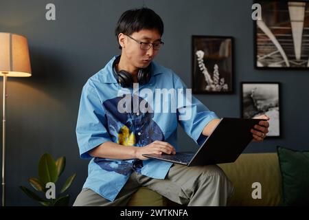 Minimal portrait of Asian young man using laptop in office lounge or at home and working in IT Stock Photo
