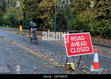 A cyclist passing a large 'Road Ahead Closed' sign on a urban road in Shepperton Surrey England UK Stock Photo