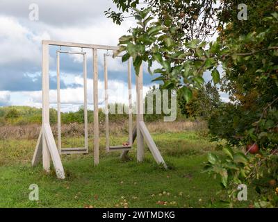 Empty wooden swing for two persons in the picturesque orchard, selective focus. Concept of motionless, relaxation, summertime leisure Stock Photo