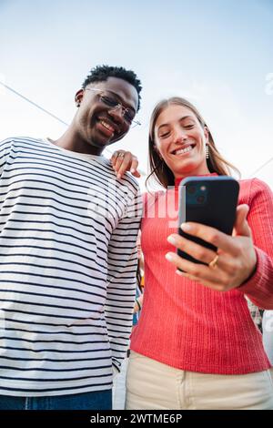 Vertical portrait of two teenage happy friends watching funny videos browsing on internet app with a smartphone and smiling together. Multiracial couple using a cell phone to post in a social media. High quality photo Stock Photo