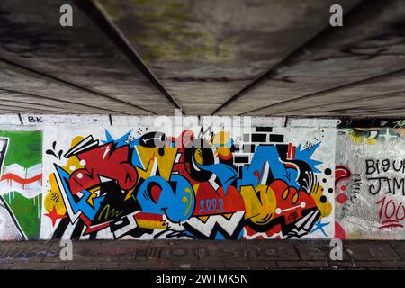 People walk past a graffiti mural under a bridge in Glasgow, Scotland. Stock Photo