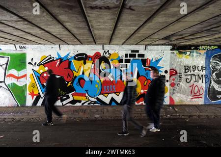 People walk past a graffiti mural under a bridge in Glasgow, Scotland. Stock Photo