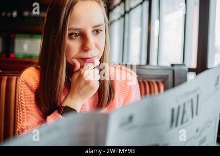 A woman is seated at a table, attentively reading a menu Stock Photo