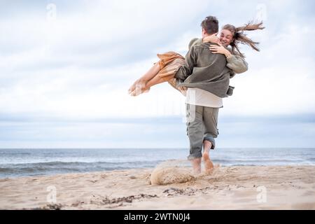 A young couple shares a joyful moment, man caring his bride both happy, their happiness as boundless as the sea behind them, celebrating love, engagem Stock Photo