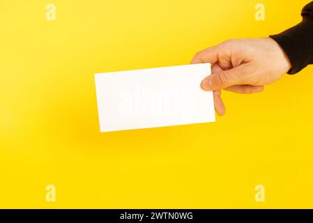 Hands with business card. Hand holding a white card on a coloured yellow background. Stock Photo