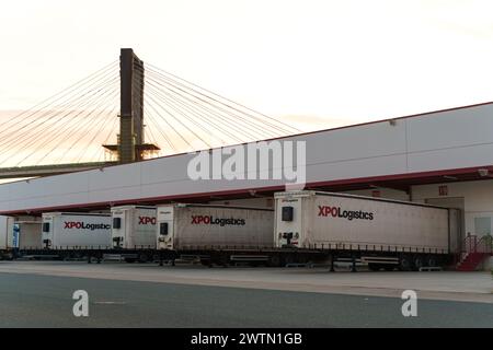 Seville, Spain - June 1, 2023: Several XPO Logistics trailers parked at a loading dock with a cable-stayed bridge in the background, captured at dusk. Stock Photo